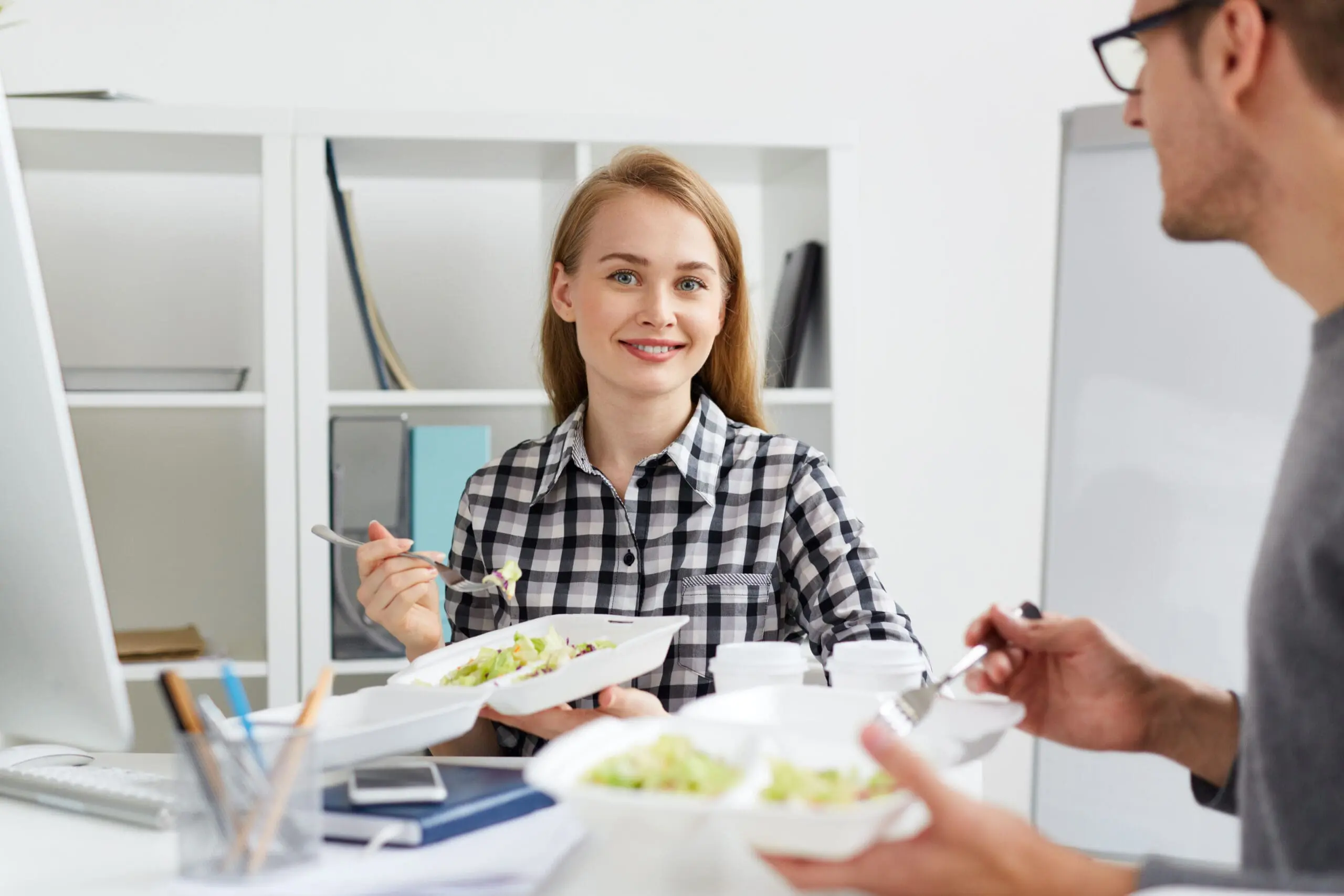 Mitarbeiterin isst gesundes Mittagessen – Ernährung als Teil von Stressmanagement im Unternehmen zur Förderung von Energie und Konzentration.